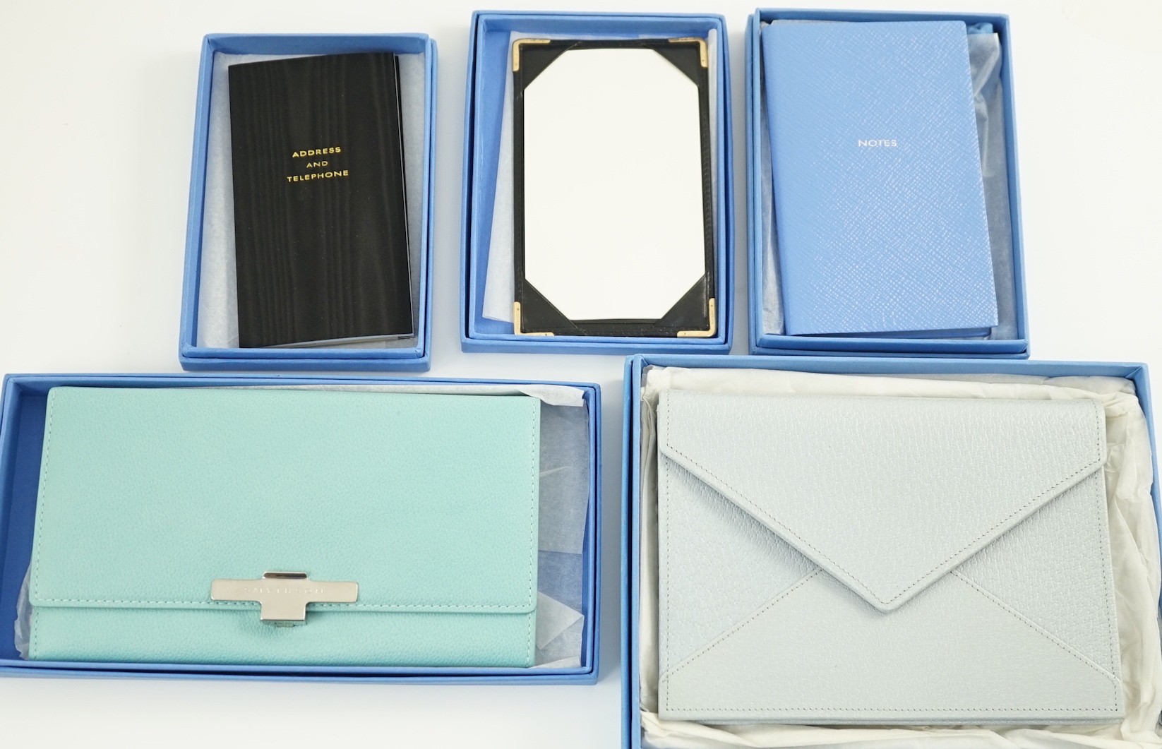 Smythson of London. A black leather notepad, 14cm, two moire silk address/telephone books, a pale grey leather purse,18cm, a Panama cornflower blue notebook, 14 cm and a duck egg blue purse, 20 cm. all boxed.